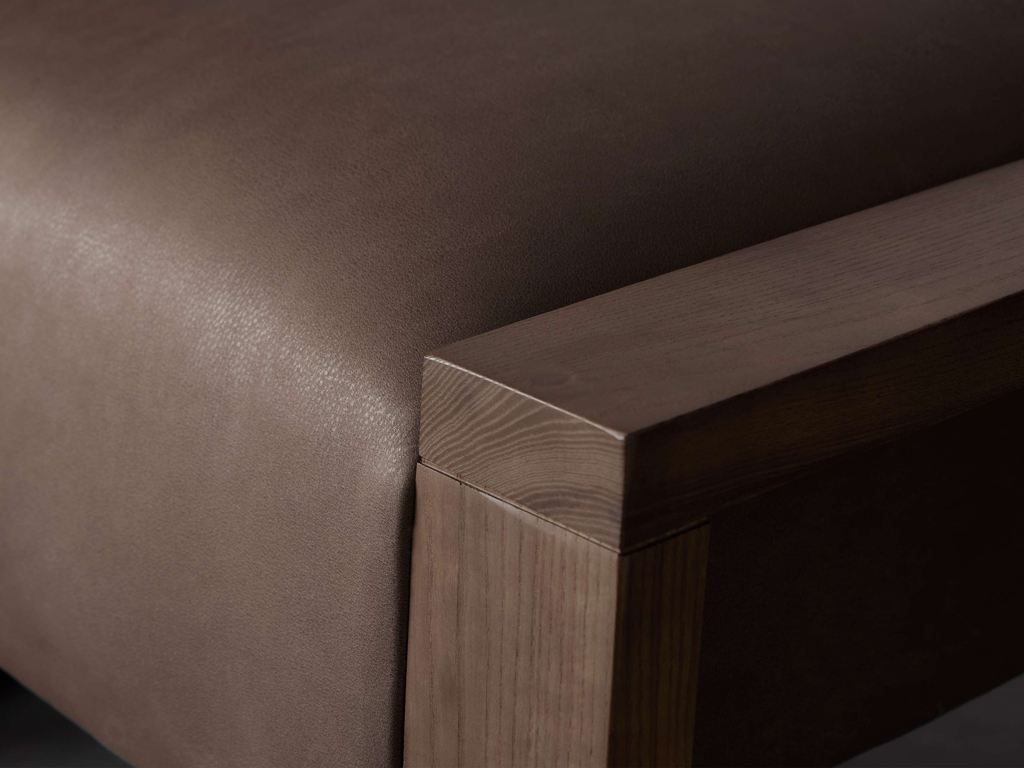 Close-up of a leather-upholstered ottoman in brown with visible wood grain on the frame, showcasing craftsmanship details.