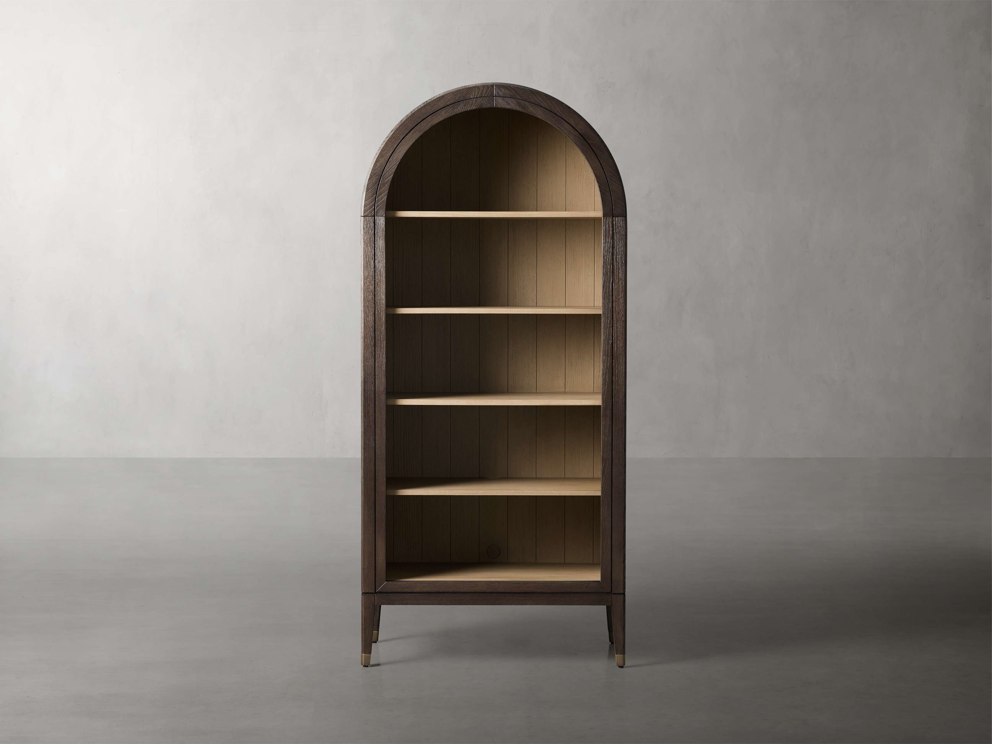 A tall, arched open bookcase made of dark oak with gold-tipped tapered legs and multiple shelves, showcased in a minimalist setting.