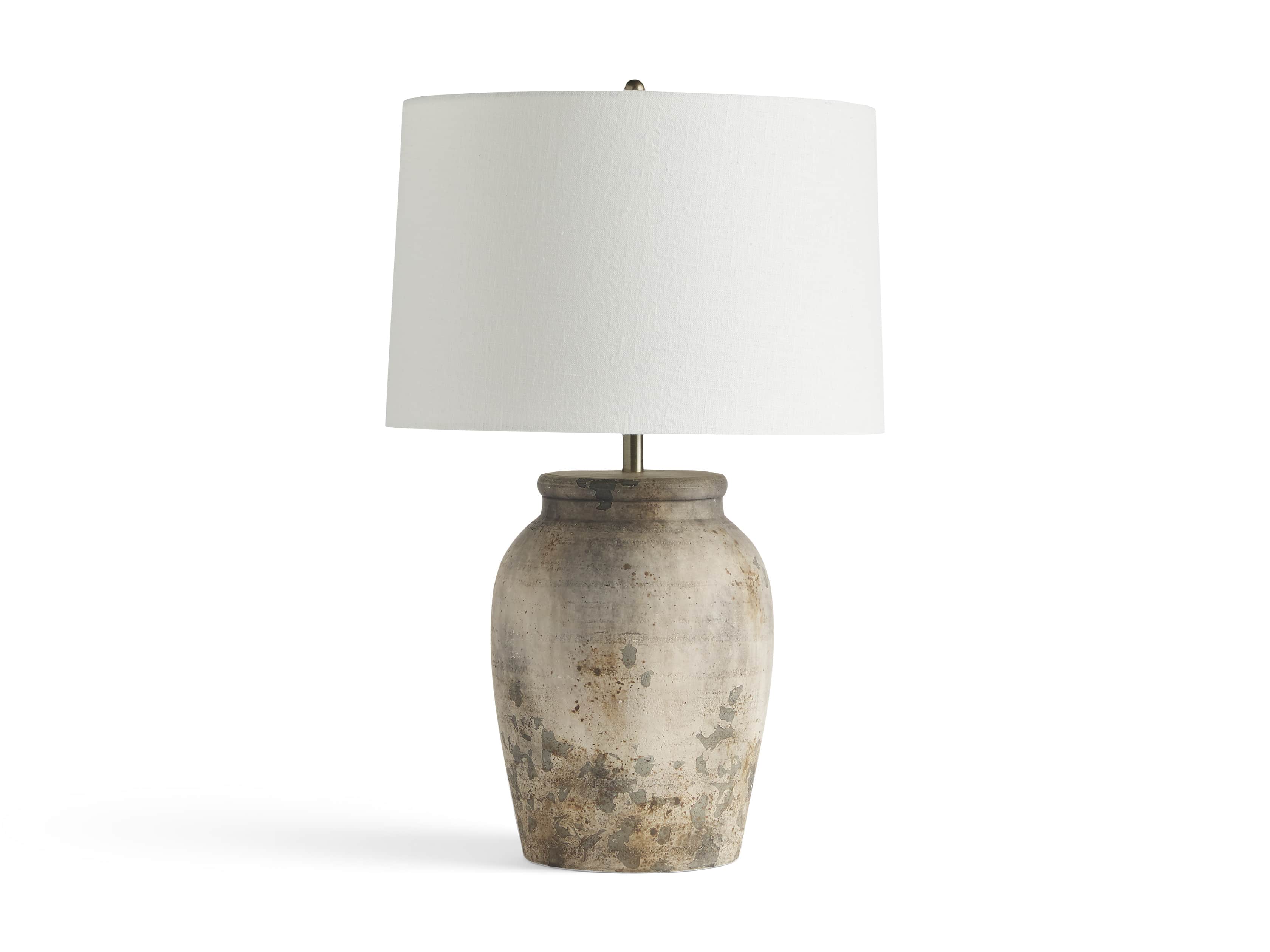 A ceramic table lamp with a hand-painted distressed gray finish, featuring an urn-shaped base and a white drum shade.
