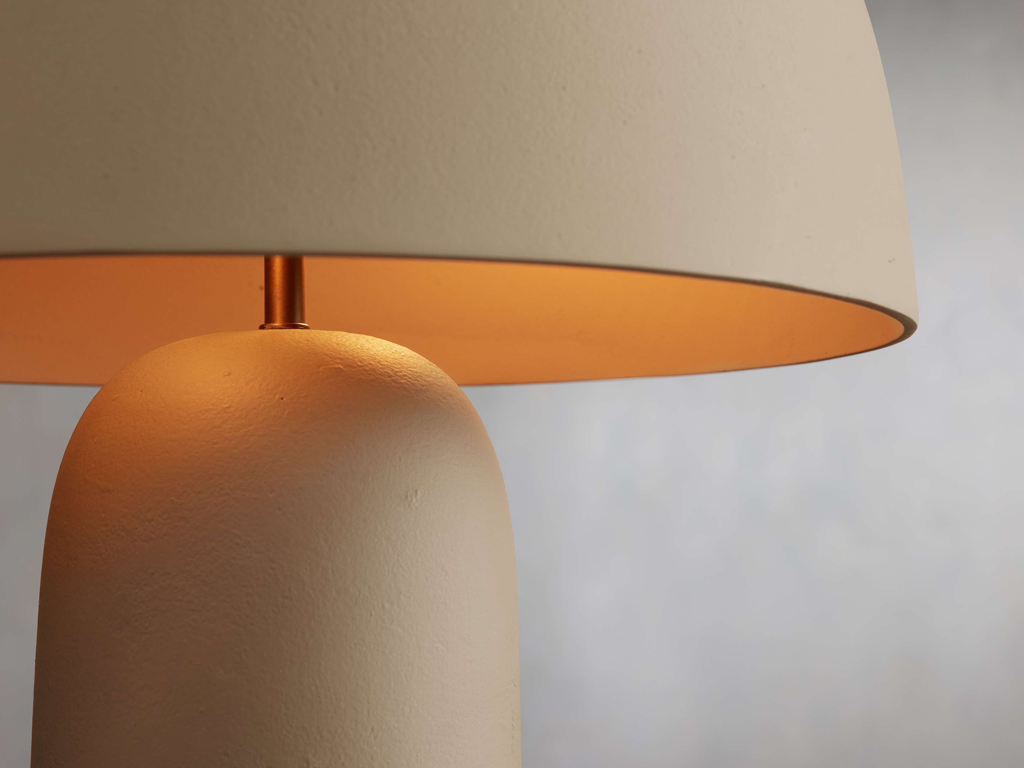 Close-up of the Ira Table Lamp in beige with a rounded base and bowl-shaped shade, softly lit with warm light.