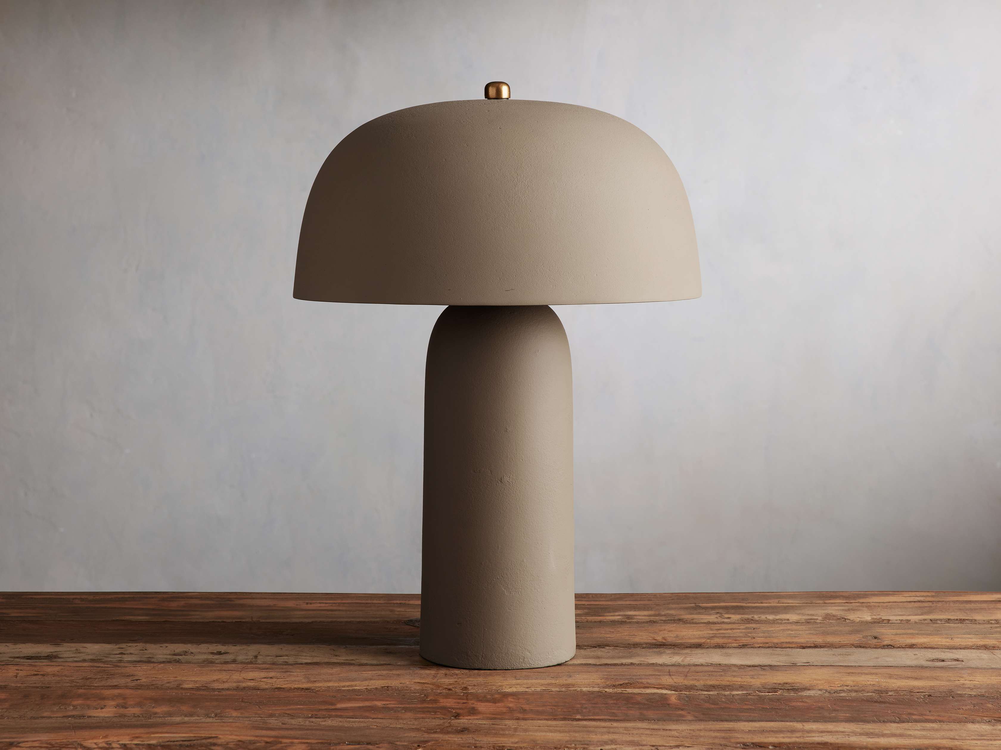 The Ira Table Lamp in brown with a mushroom-style shade and cylindrical base, featuring a gold knob on a wooden surface.