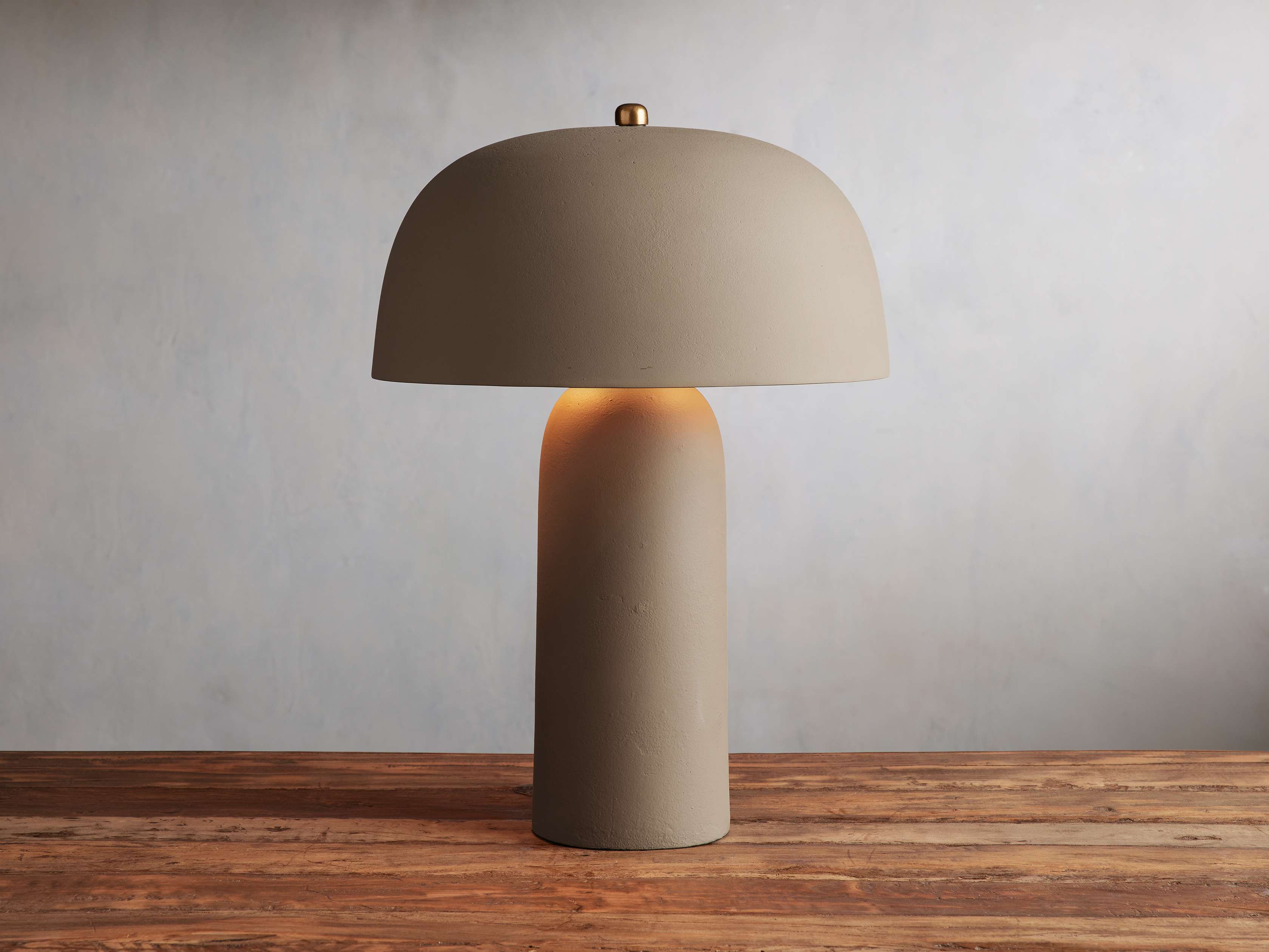 Ira Table Lamp in brown featuring a mushroom-style beige shade and cylindrical base, placed on a wooden surface.