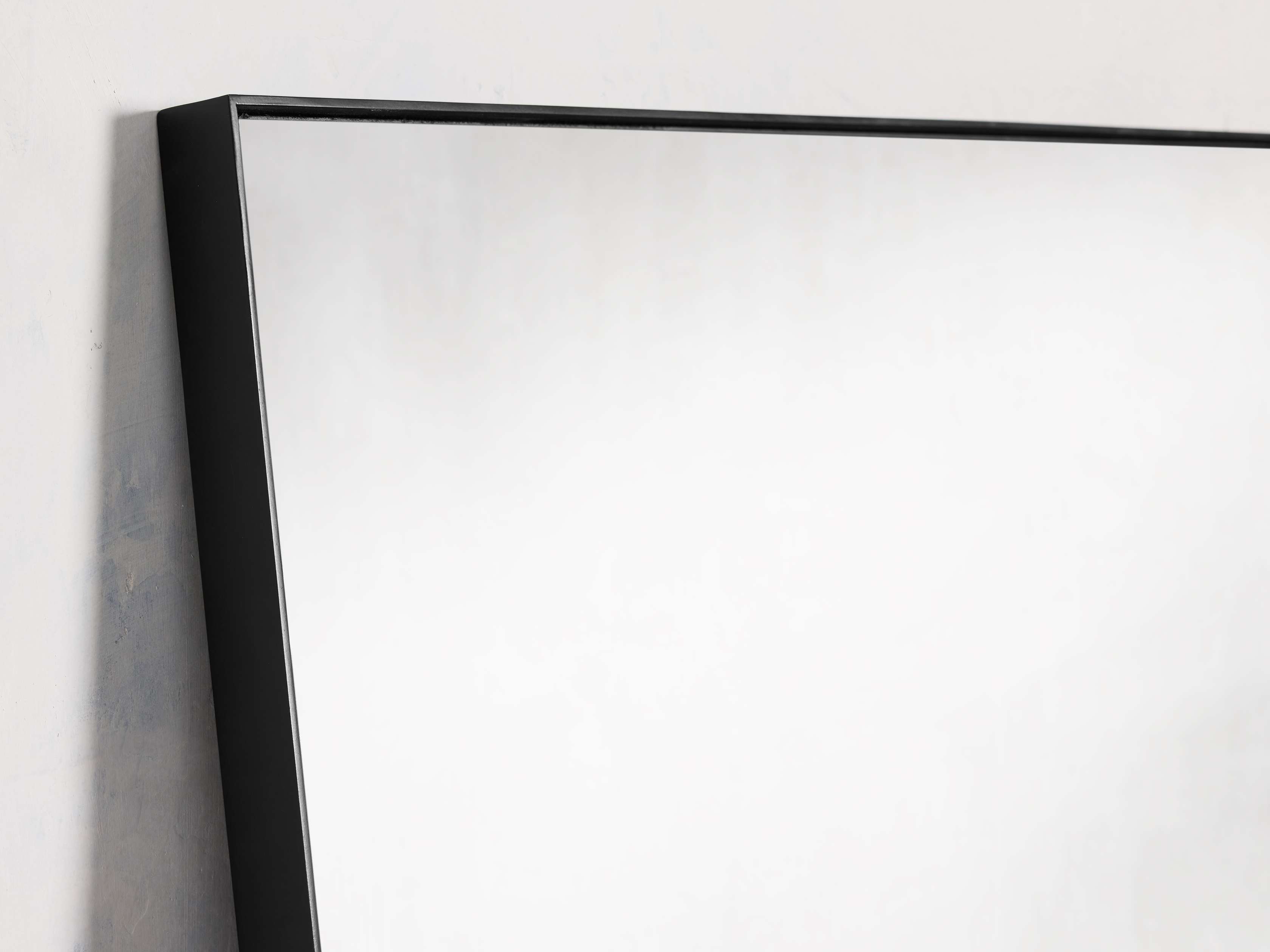 Rectangular floor mirror with a minimalist black steel frame, leaning against a wall.