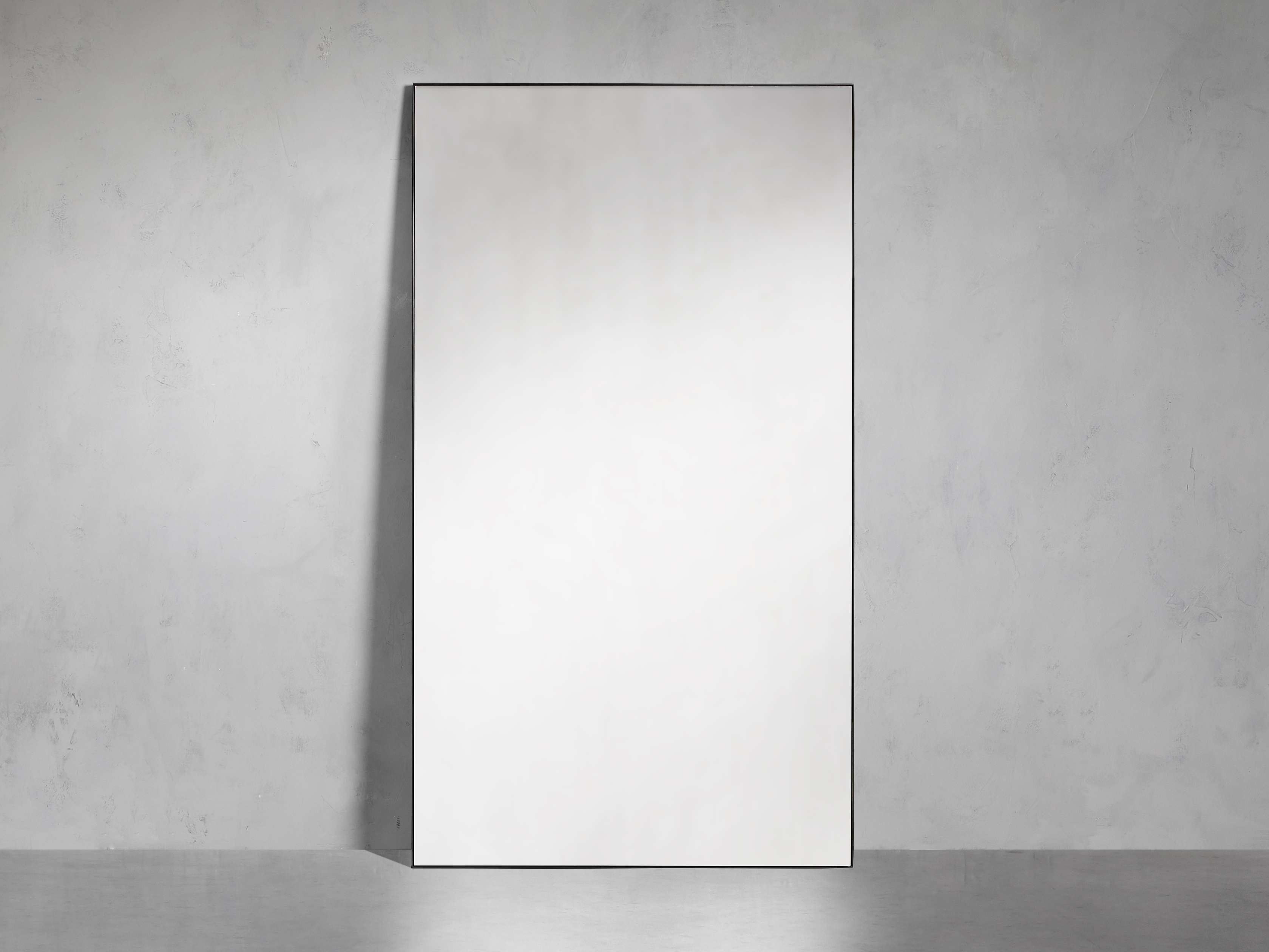 Rectangular Lira Grand Floor Mirror with a minimalist black steel frame leaning against a light gray wall.
