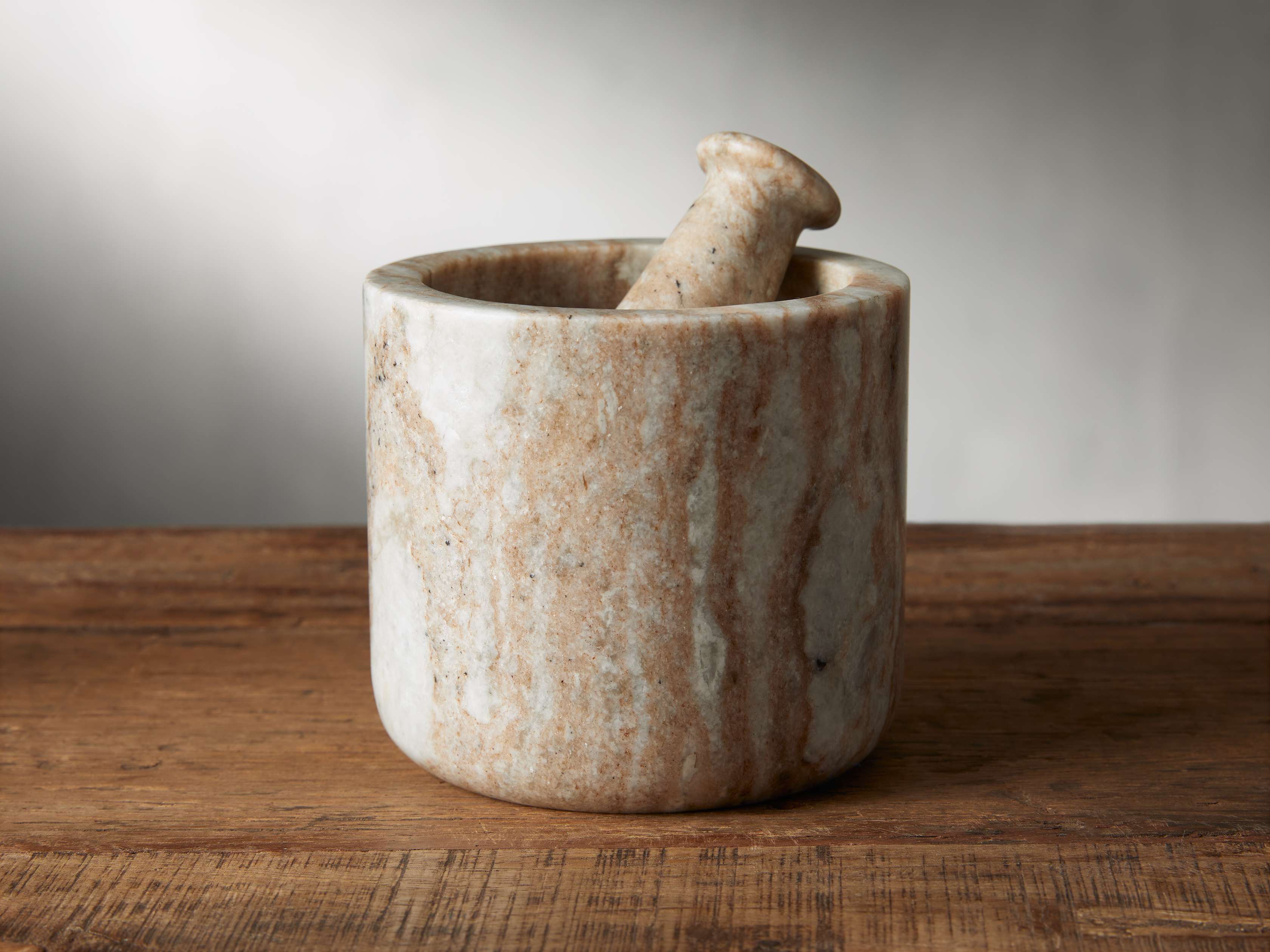A brown marble mortar and pestle with cream and ivory veining, displayed on a wooden surface against a neutral background.