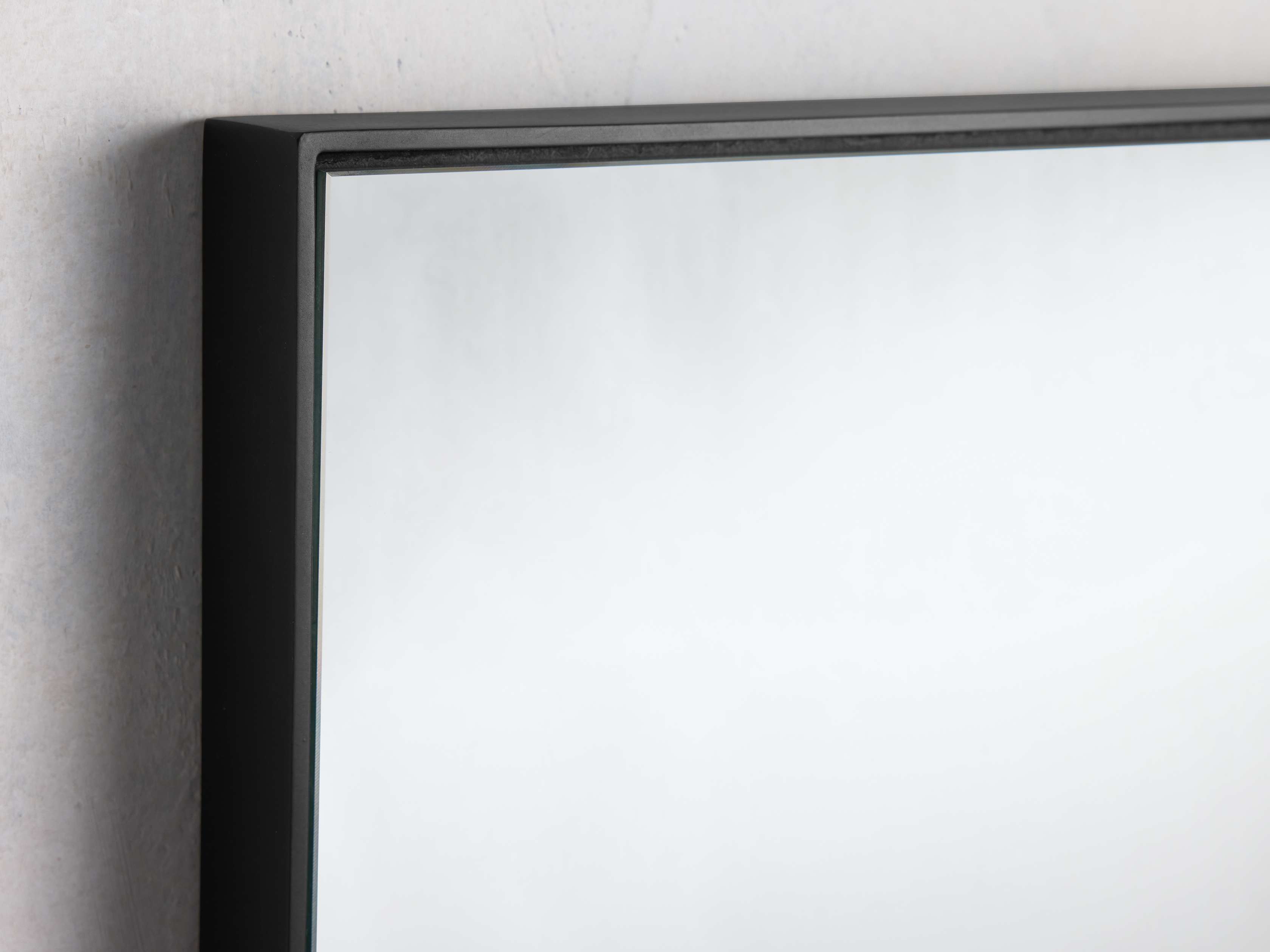 Close-up of the Lira Wall Mirror in Black, showcasing its minimalist steel frame and sleek rectangular design against a light wall.