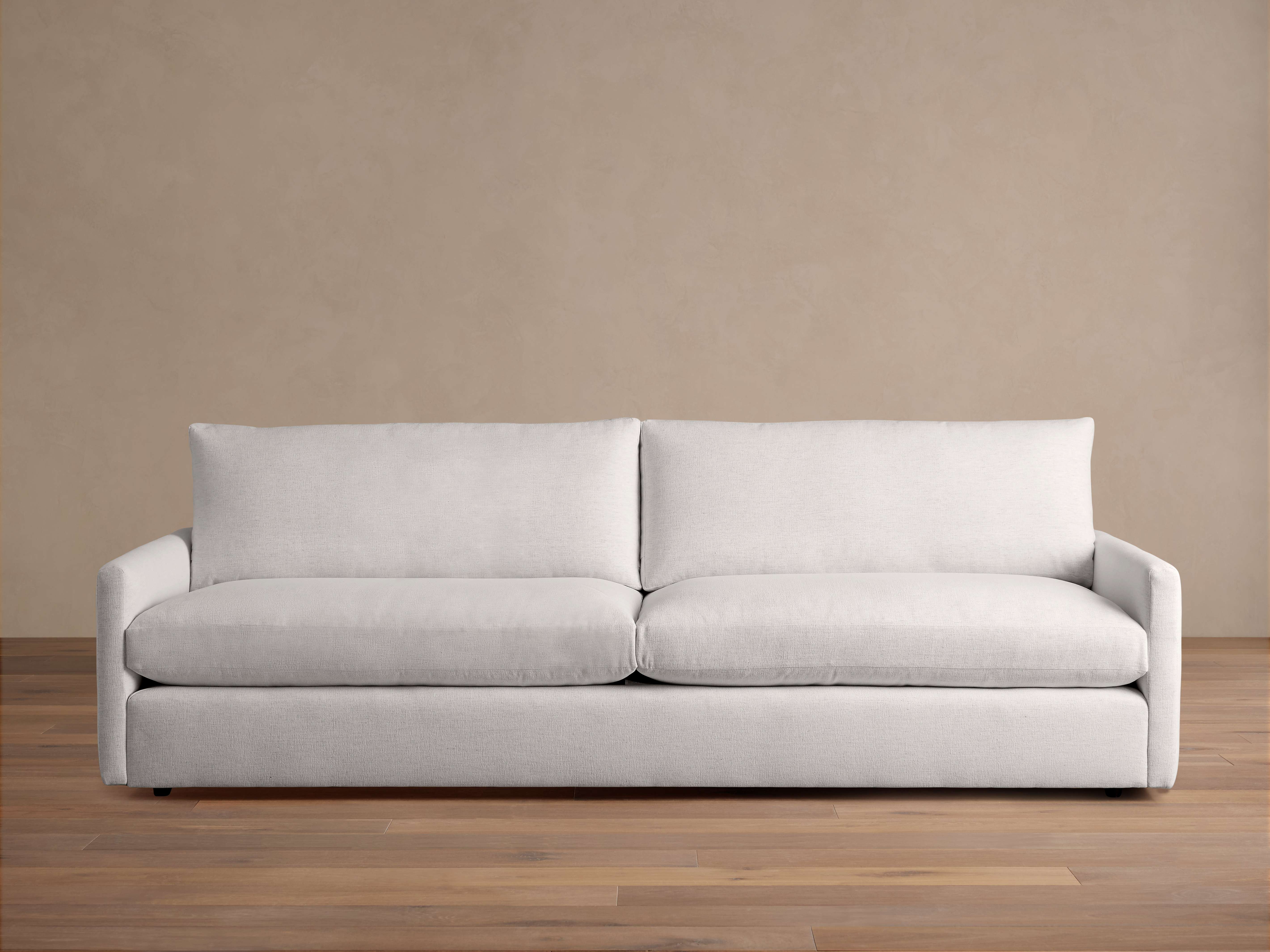 Kipton Sofa in light gray fabric, features a modern design with straight arms, plush seat and back cushions. Placed on wooden floor.