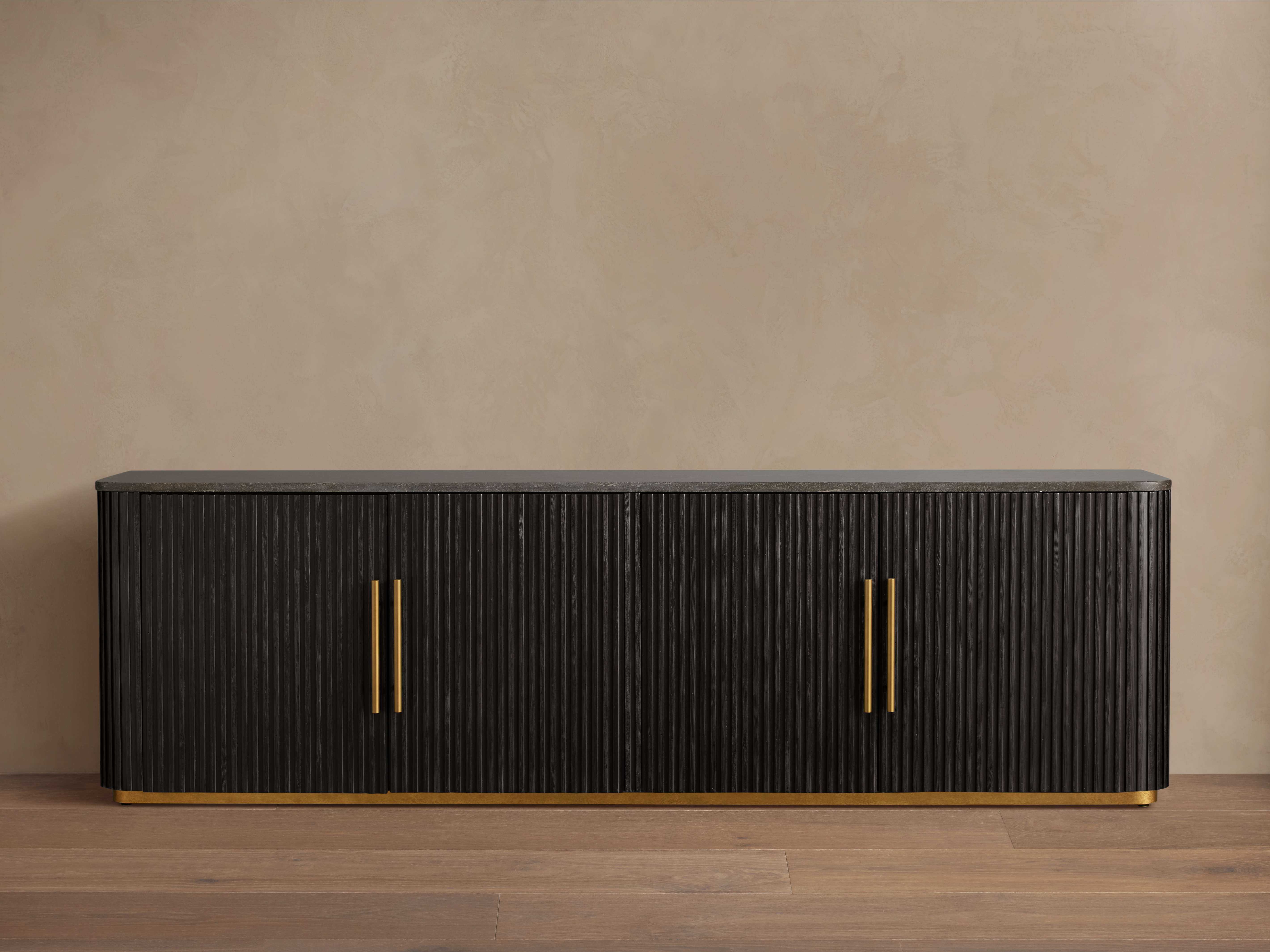 Finnley Media Console in dark finish with ribbed texture, four doors, and brass zinc-alloy edge pulls. Sits on wooden floor.
