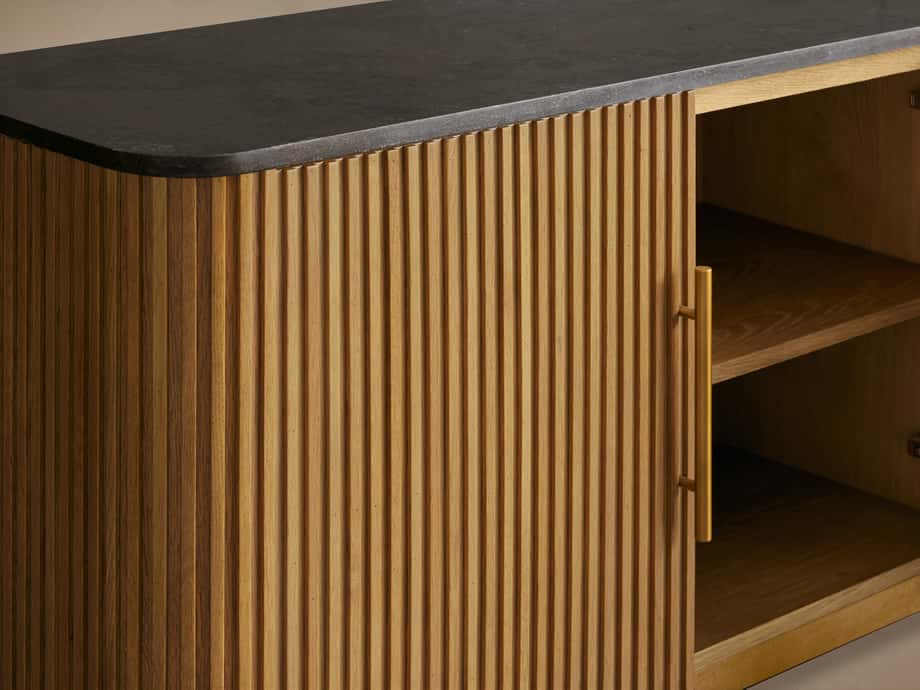 Finnley Media Console featuring a ribbed oak wood front, black stone top, open shelves, and brass-finished handles.