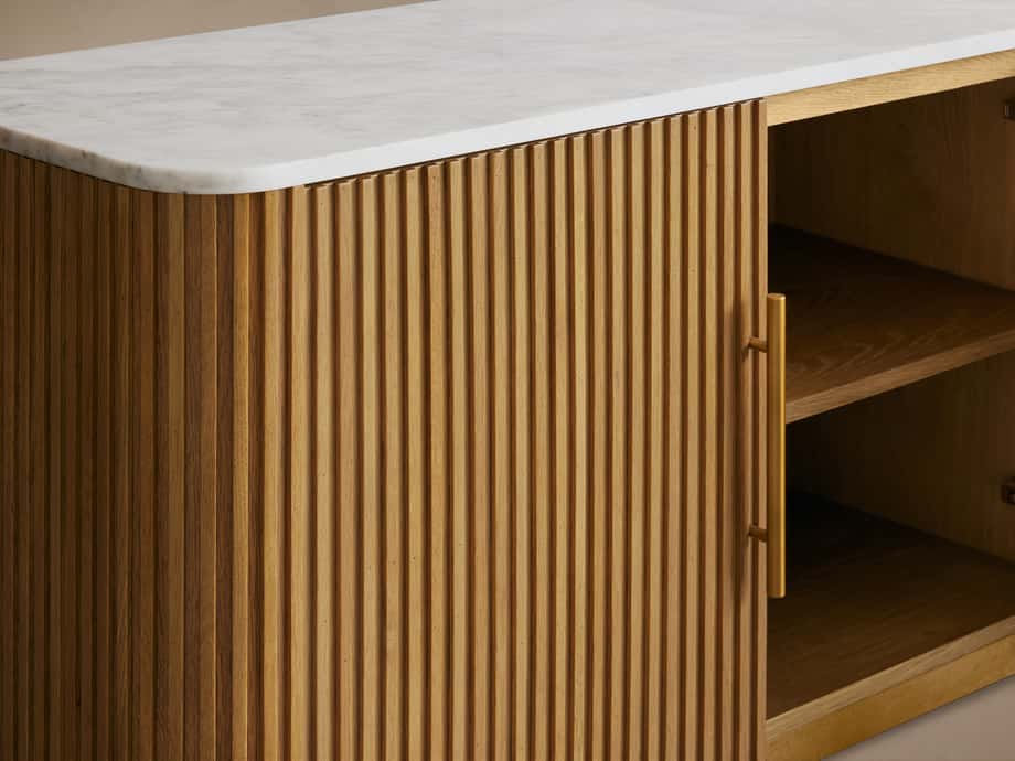 Finnley Media Console with vertical wood slats, light honey finish, white marble top, and brass-finished pull handle.
