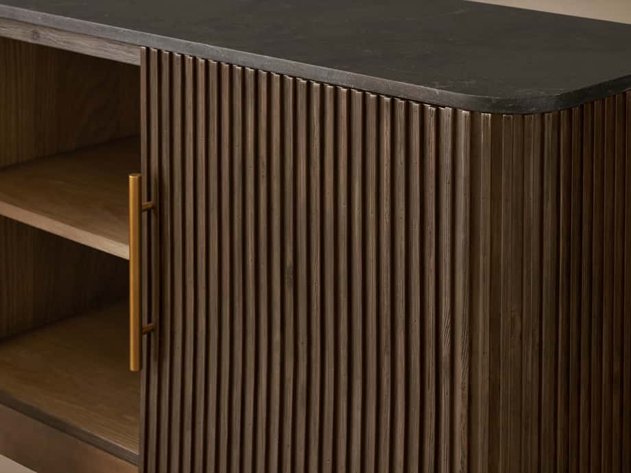 Finnley Media Console with dark stone top, ribbed wood front, brass handle, and open shelving on the left side.