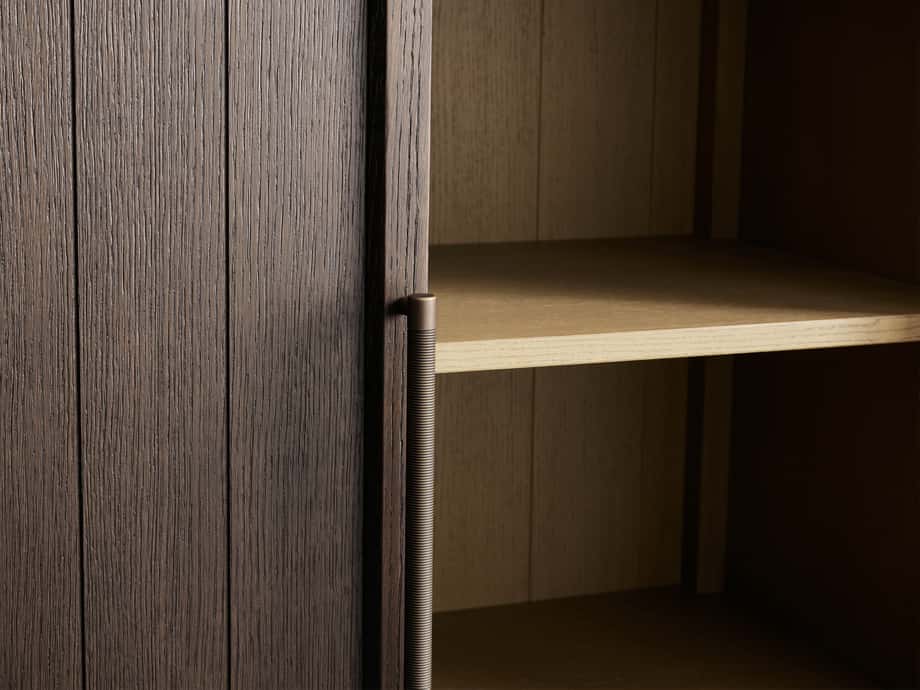 Close-up of the Hattie Cabinet's dark oak wood finish showing a reeded handle, open door, and visible adjustable shelves inside.