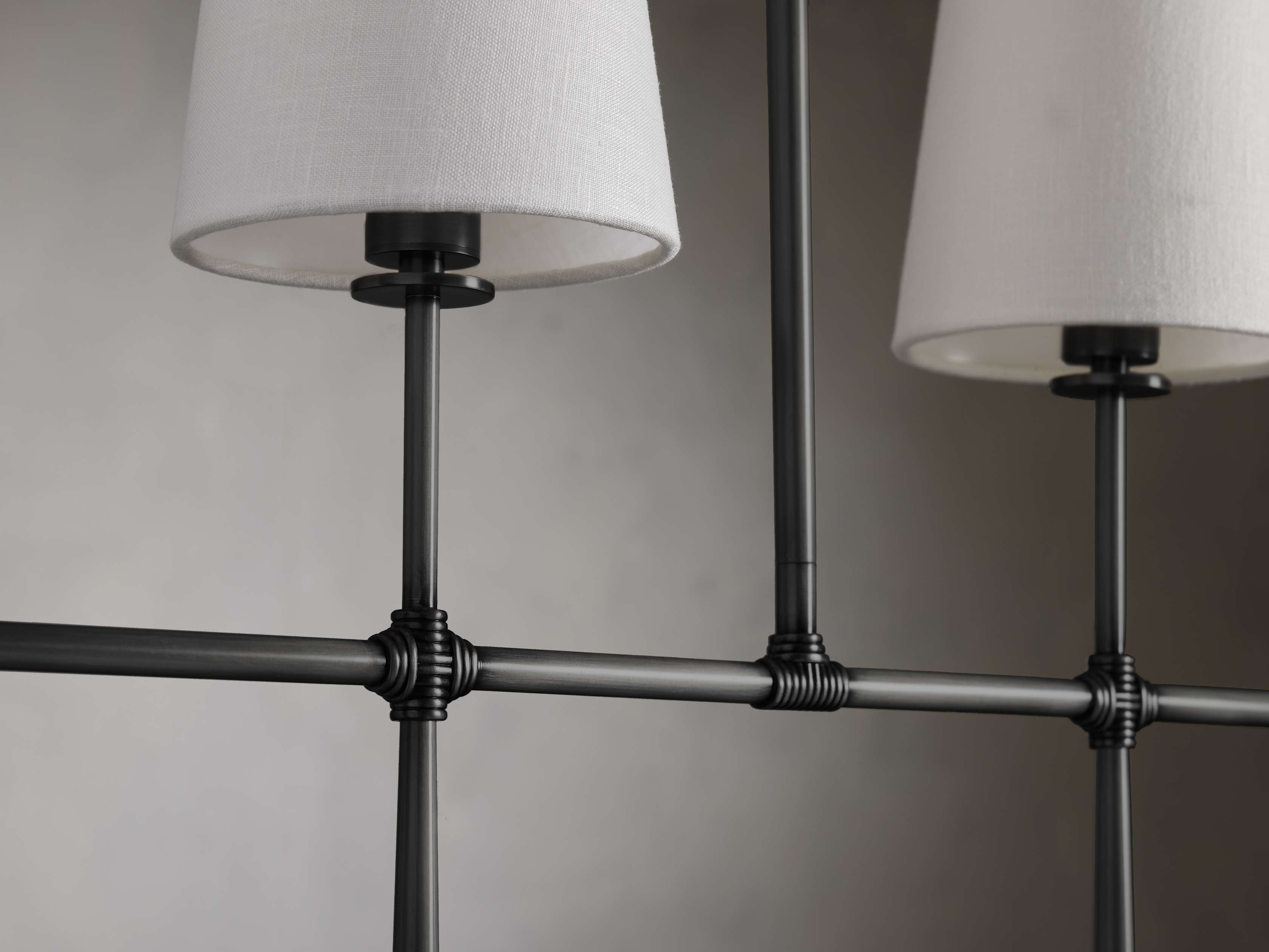 Rhodes Linear Chandelier in bronze with black metal rods and white tapered linen shades against a neutral background.