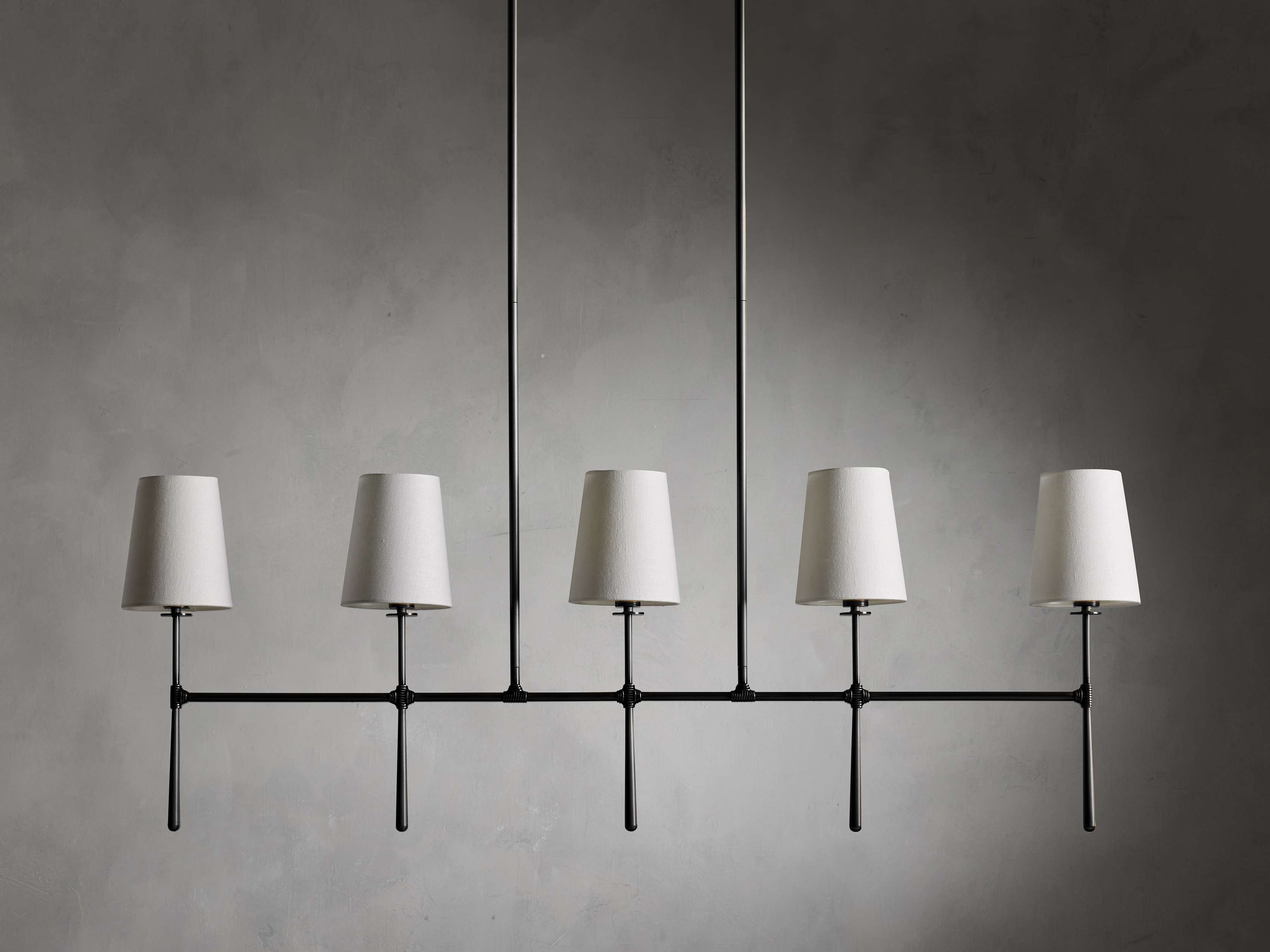 Rhodes Linear Chandelier with black steel frame, five white tapered linen shades in a horizontal line against a gray background.