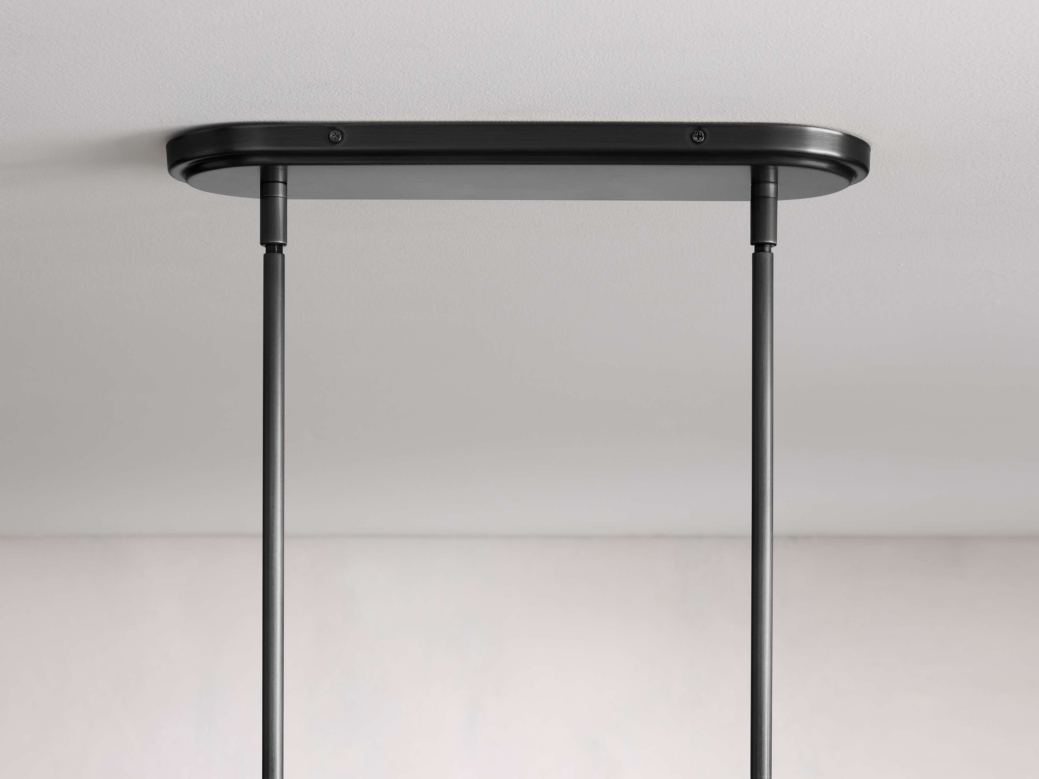 Black ceiling mount with two hanging rods, part of the Rhodes Linear Chandelier, set against a light background.