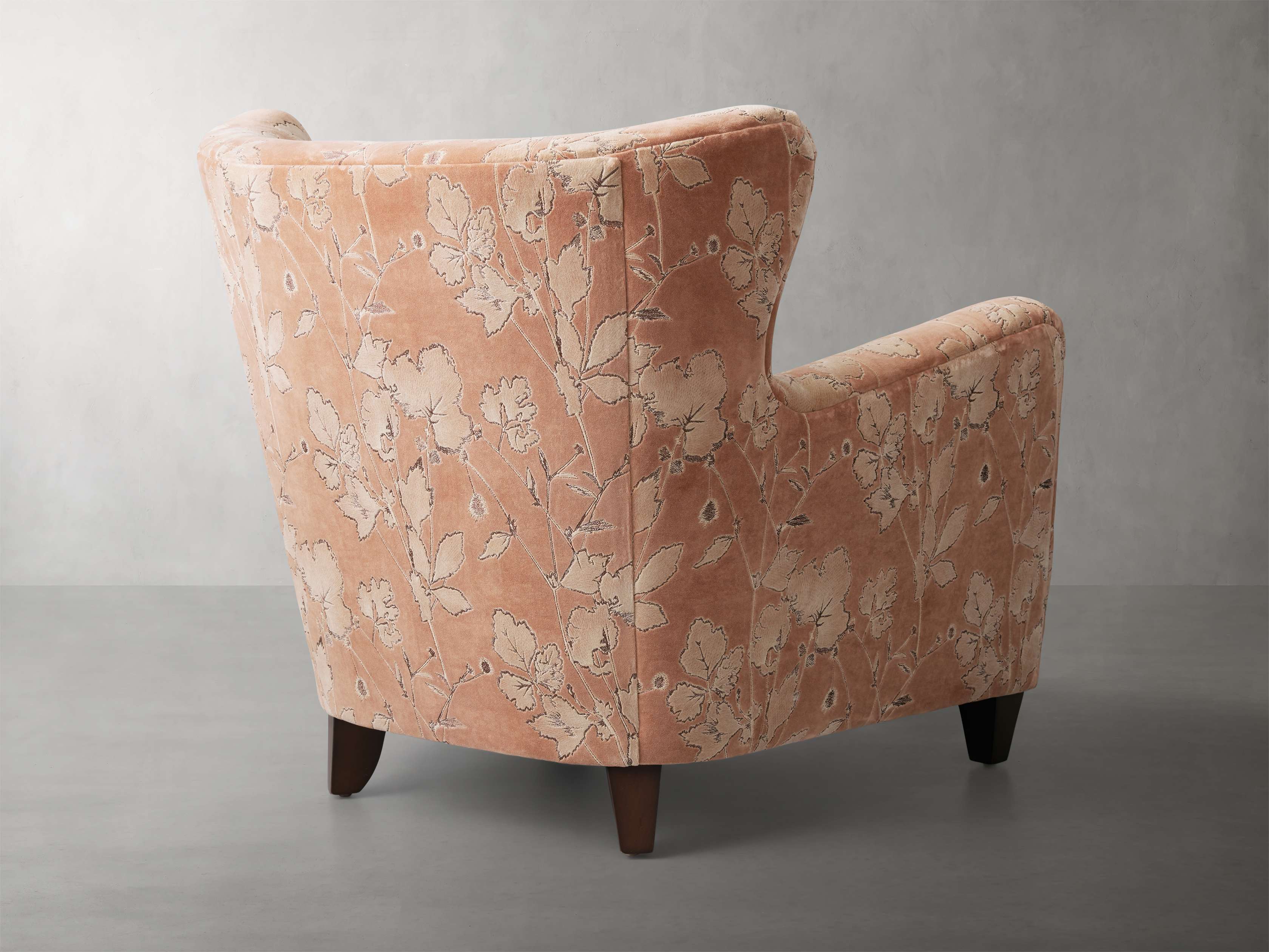 The back of a peach-colored armchair with a floral pattern, shown from an angle.
