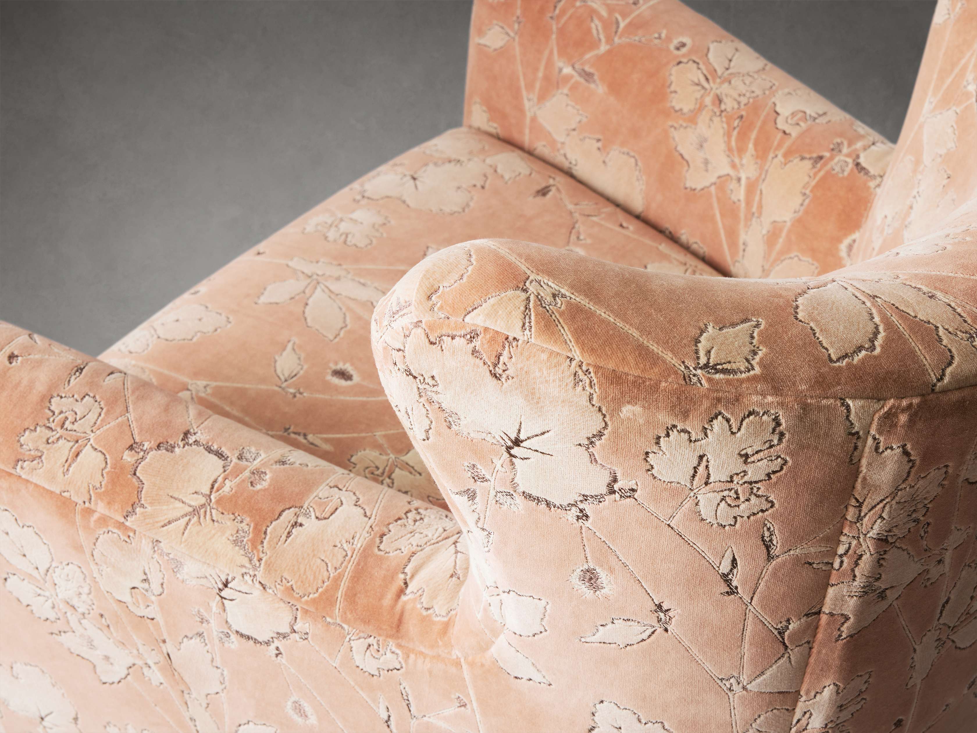 A close-up of a peach-colored armchair with a floral pattern, focusing on the arm and seat cushion.